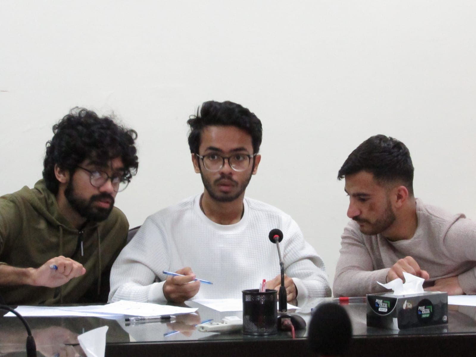 Participants sit at a table with microphones and answer sheets.